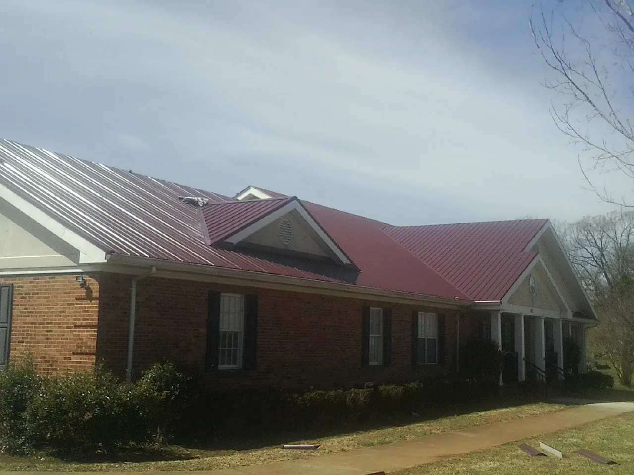 Red metal roof with gabled entries on a long brick building, from a Hail Damage Roof Repair job in Coalmont