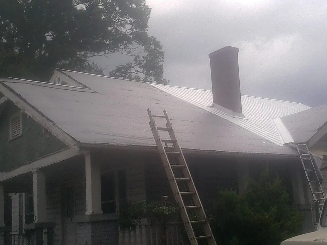 Ladders against a metal roof on an older home with a brick chimney in Coalmont